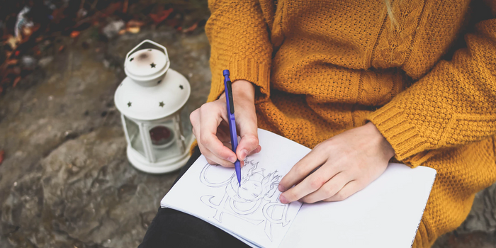 femme dessinant sur un cahier avec un pull orange